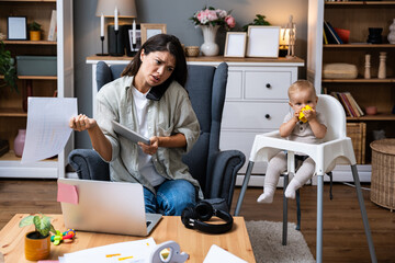 Overwhelmed work from home mom juggles phone call laptop and paperwork while monitoring baby in high chair multitasking through billing issues deadline and support queues striving to stay professional
