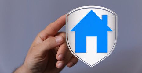 A hand holding a house icon within a shield, symbolizing security, protection, and home ownership....