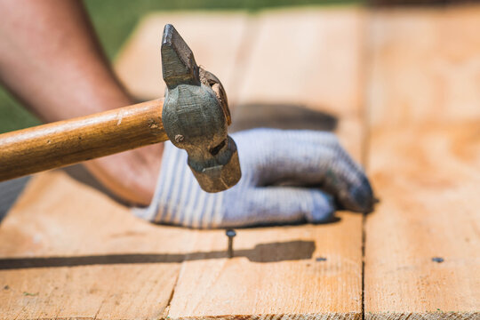 A carpenter in cloth protective gloves nails wooden planks. Close-up of a nail hammered into a board.