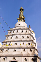 The stupa is a white, multi-tiered structure topped with a golden spire with eyes. Prayer flags wave in the breeze against a clear blue sky at Swayambhunath in Katmandu.