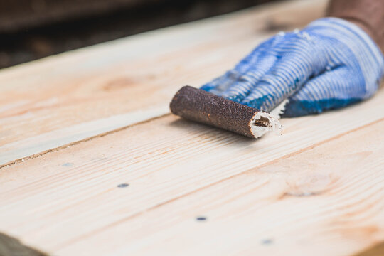 The concept of DIY woodworking and construction. A carpenter wearing cloth gloves manually polishes wooden boards with sandpaper for grinding. - Powered by Adobe