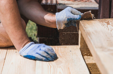The concept of DIY woodworking and construction. A carpenter wearing cloth gloves manually polishes wooden boards with sandpaper for grinding.