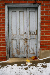 Vieille porte en bois avec des feuilles d'érable et de la neige au sol , avec un mur de briques en arrière-plan.