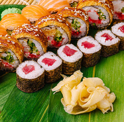 Colorful sushi rolls arranged on a green leaf with ginger garnish