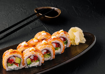 Colorful sushi rolls served on a dark plate with ginger and soy sauce