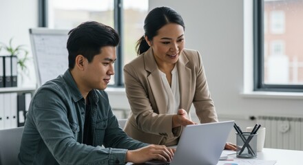 Asian male and female colleagues collaborating on laptop in modern office