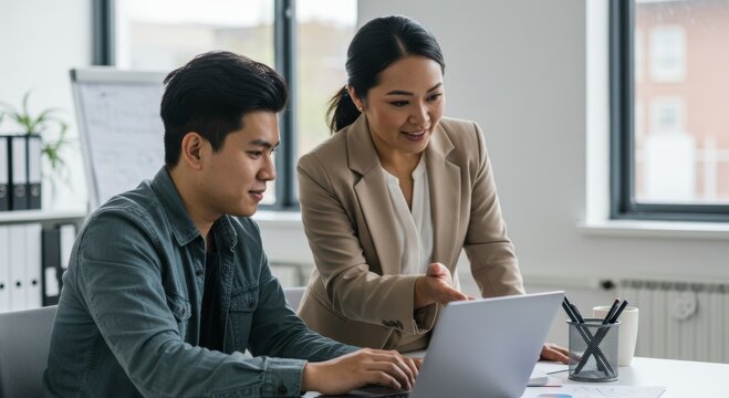 Asian male and female colleagues collaborating on laptop in modern office