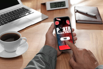 Man playing online poker on mobile phone at wooden table, closeup