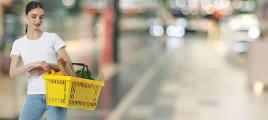 Woman holding shopping basket with different food products at supermarket. Banner design