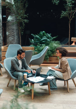 startup pitch rehearsal in cozy lounge, practicing investor presentation with printed deck and laptop, mentor