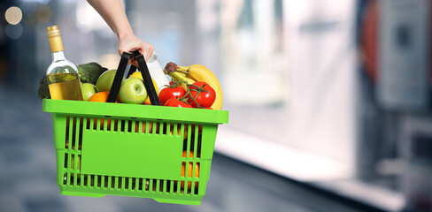 Customer holding shopping basket with different food products at supermarket, closeup. Banner design