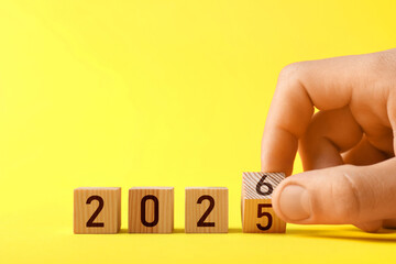 New Year. Man flipping cube with numbers 5 and 6 to make 2026 on yellow background, closeup