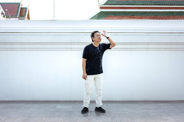 Thai man pours drinking water over his face to cool down under the intense Bangkok heat. Standing...