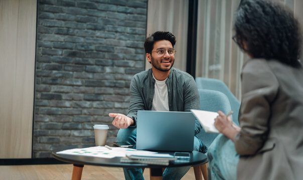 man and woman collaborating over laptop, energetic pitch and discussion with notes on table, casual meeting