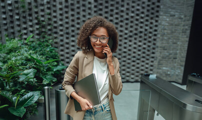 woman scanning access card at turnstile holding portfolio, smiling arrival in lobby with modern architecture