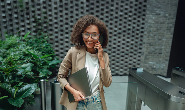 woman scanning access card at turnstile holding portfolio, smiling arrival in lobby with modern architecture