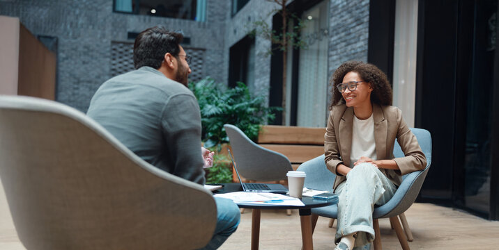two professionals meeting in atrium over coffee and documents, exchanging roadmap ideas and strategic feedback - Powered by Adobe