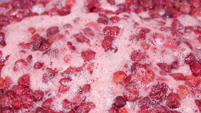 Large quantity of cut strawberries bubbling in pinkish foam during domestic confiture preparation.