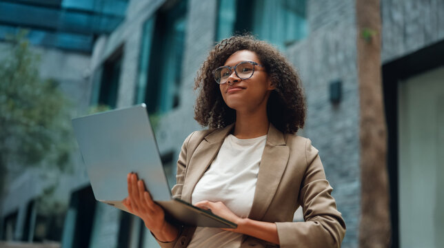 diverse female teamlead presenting laptop screen with poised confidence, office atrium backdrop, business