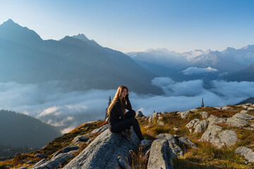 A woman gazes out over a mountain view as she sits on a rocky outcrop.
