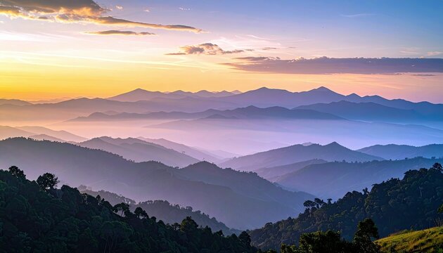 A breathtaking landscape of layered mountains shrouded in mist, illuminated by the soft, colorful glow of a sunrise.