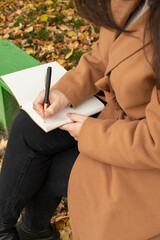 Woman in brown coat sitting on bench and writing in notebook	