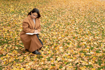 Young attractive woman in brown coat writing in notebook