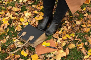 Legs ow a woman, bag,  brown-covered notebook and a pen
