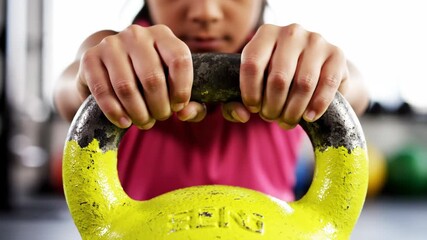 Woman's hands gripping a yellow kettlebell in a gym, close-up showing strength, focus and dedication to weight training, fitness routine and active healthy lifestyle