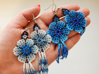 A human hand holds an earrings in the form flower, a boho element