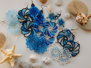 Blue earrings in the shape of flower on a white background with sea pebbles