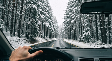 First-person view of driving a car on a winding road through a snowy winter forest. A driver's hand on the steering wheel during a cold weather road trip