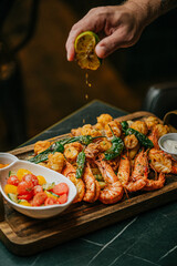 A plate of food with shrimp, tomatoes, and lime. A person is pouring lime juice over the shrimp