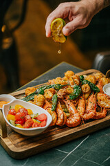 A plate of food with shrimp, tomatoes, and lime. A person is pouring lime juice over the food