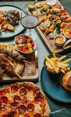 A table with a variety of food and drinks, including pizza, chicken, and fries. The table is set for a meal, and there are wine glasses and cups on the table as well. Scene is inviting and cozy