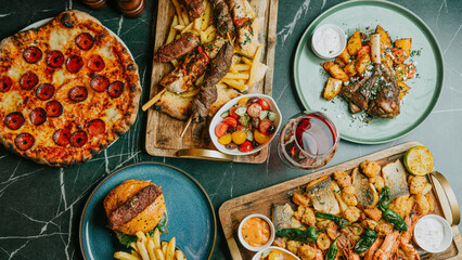 A table full of food including pizza, chicken, and fish. The table is set for a meal © Reuben