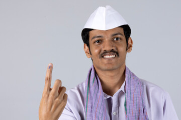 Indian young marathi man showing ink marked finger by looking at camera after voting on election - concept of people voting rights, democracy and happiness against studio background 