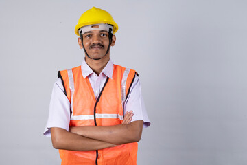 Close shot of a indian man engineer worker arm crossed and wearing safety uniform and yellow engineer cap. worker looking at camera isolated on studio grey background