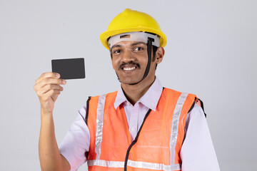 Close shot of a indian man engineer worker showing Aadhar card and wearing safety uniform and yellow engineer cap. worker looking at camera isolated on studio grey background