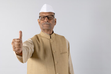 Portrait of Indian politician man  showing thumbs and looking in front of the camera wearing  kurta pajama and politician cap. Concept of political leader in india.