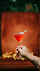 A person is holding a martini glass with a pink drink in it. The drink is garnished with a strawberry. Concept of sophistication and elegance, as the person is holding the martini glass with a smile