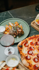 A plate of food with a glass of wine on a table. The food includes a pizza with pepperoni and a side of vegetables