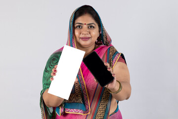 Indian rural woman showing Aadhar Card and smartphone empty screen isolated on gray studio background. Rural woman showing Government identity proof on studio background 