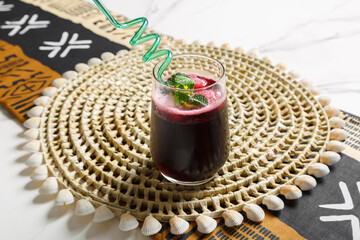 Jus de bissap dans un verre avec paille colorée, présenté sur un set de table tissé africain – boisson traditionnelle africaine.
