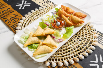 Mix d’entrées à partager : pastels et samoussas, présenté sur une ardoise et un set de table tissé africain – plat traditionnel africain. Apéritif africain