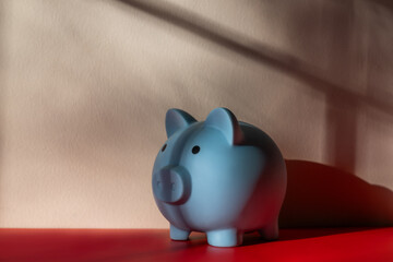 Blue piggy bank against a wall with a long shadow