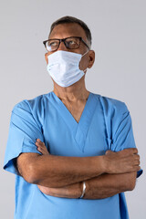 Portrait of a indian senior physiotherapist arm crossed in light blue gown and face mask deep thinking isolated studio background. Protect yourself and others medical advice against the covid-19