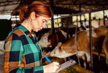 Female farmer managing a cattle barn with a male worker, making notes on clipboard.
