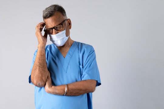 Portrait of a indian physiotherapist in light blue gown and face mask deep thinking isolated studio background. Protect yourself and others medical advice against the covid-19