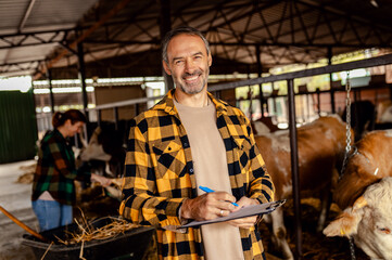 Fototapeta premium Male farmer managing a cattle barn with a female worker, making notes on clipboard.